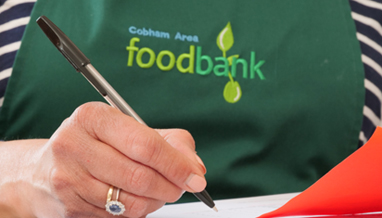 Cobham Area Foodbank volunteer holding pen and foodbank voucher